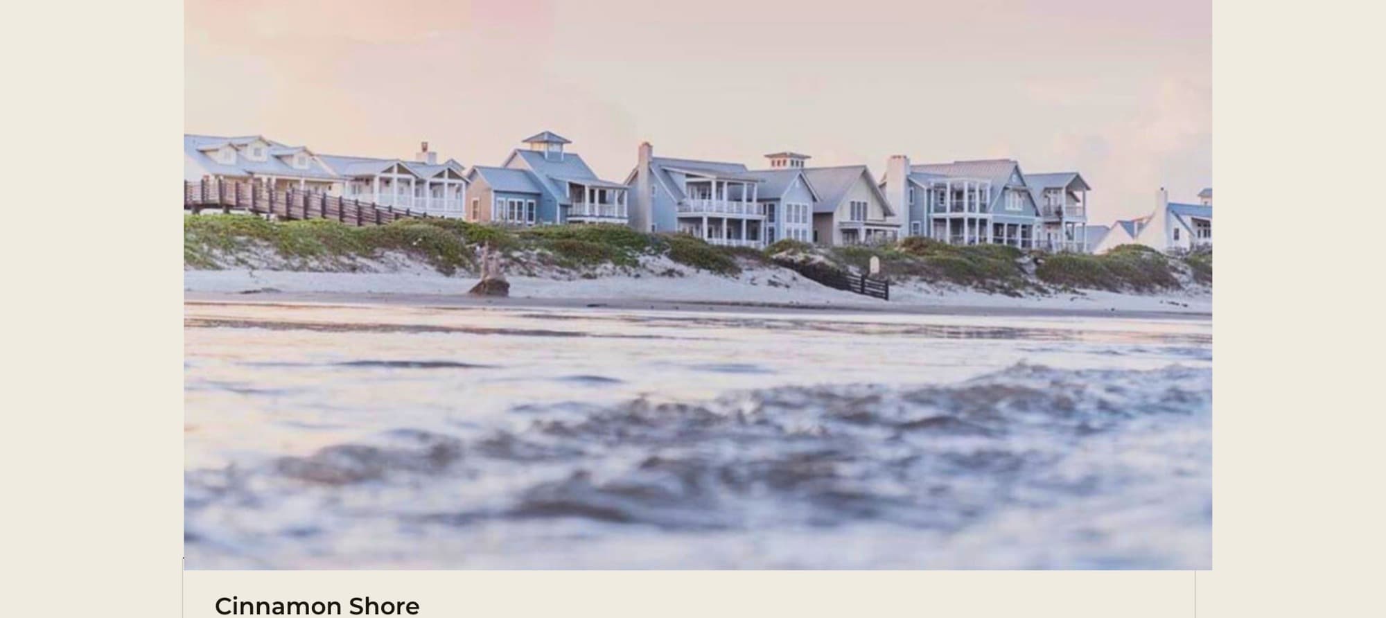 Cinnamon Shore — pastel sunset over the coastal community, beach houses behind dunes with surf in the foreground