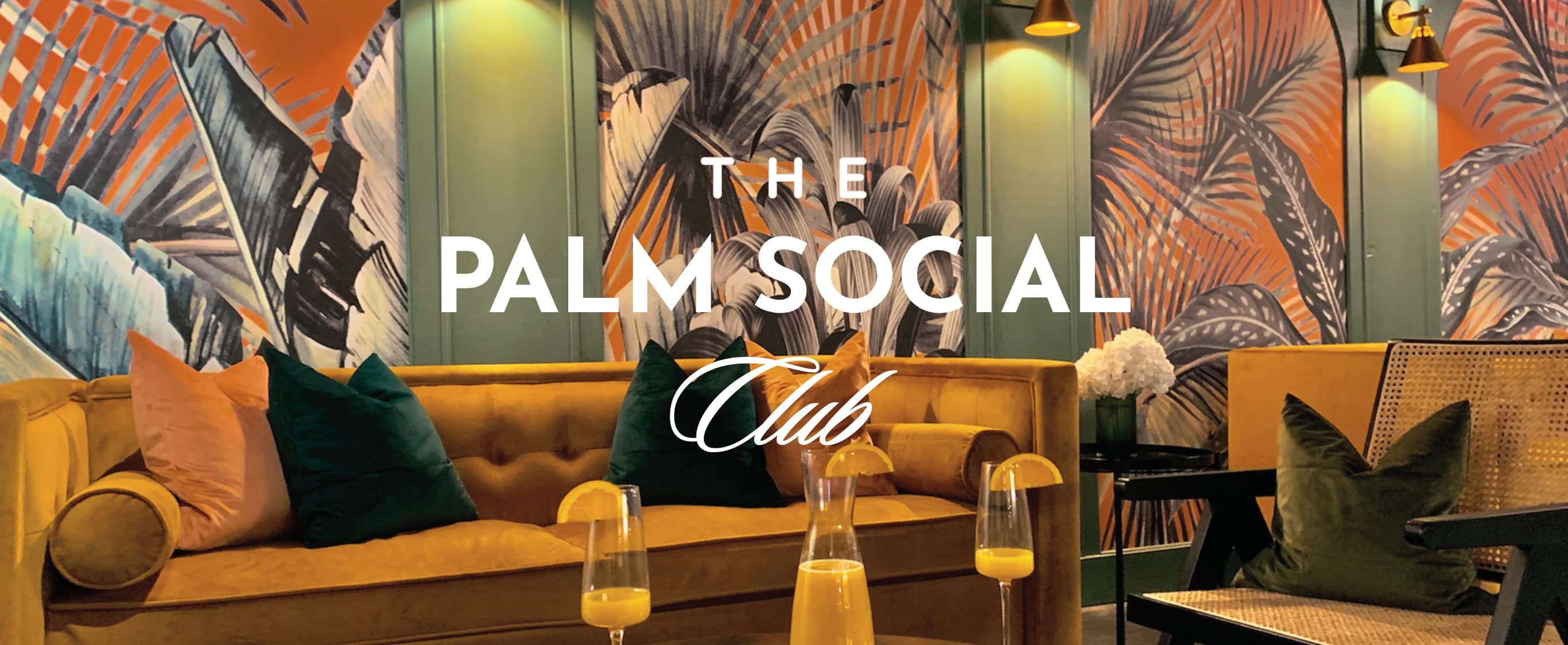 The Palm Social Club — tropical-wallpaper lounge interior with velvet sofa, throw pillows, mimosas on the table, and the PSC wordmark overlaid