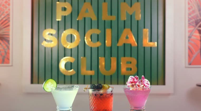 The Palm Social Club — green wood-slat sign with gold lettering and three signature cocktails on the bar